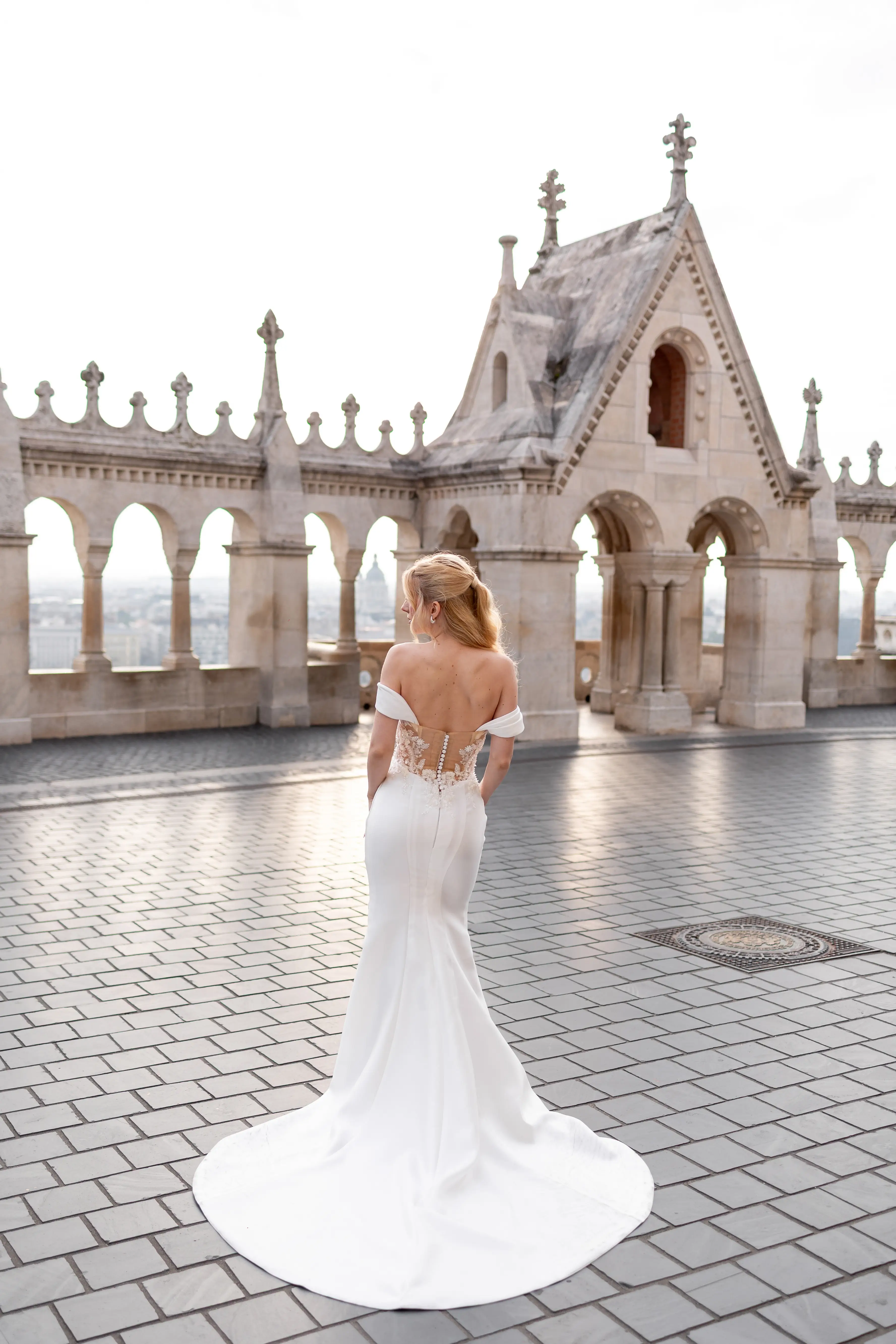 Egy menyasszony egy fehér, gyöngyökkel díszített esküvői ruhában áll egy virágokkal teli szalonban