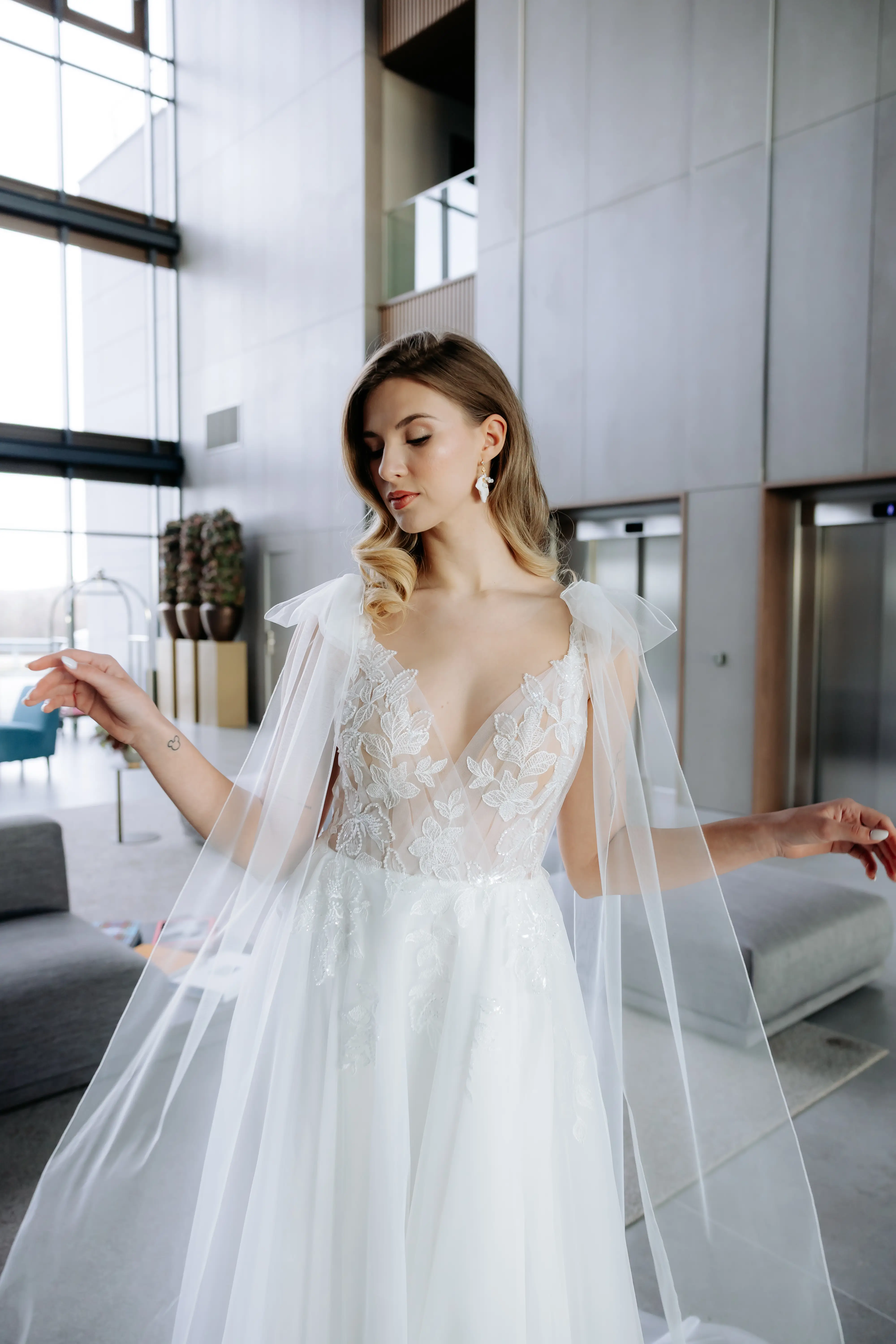 Női menyasszonyi ruha próbája egy próbafülkében, a menyasszony mosolyogva nézi magát a tükörben.